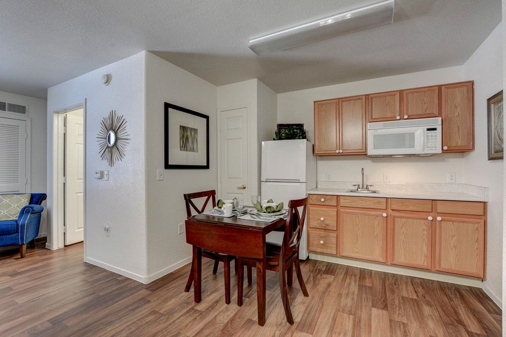 A cozy kitchen and dining area featuring a small wooden table with chairs, adjacent to a refrigerator and microwave.