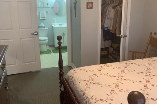 A cozy bedroom with a floral quilt, leading to an adjacent bathroom and closet.