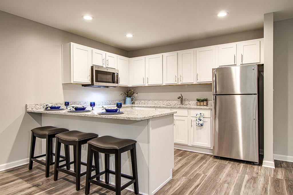 A modern kitchen featuring white cabinetry, stainless steel appliances, and a stylish kitchen island with bar stools.