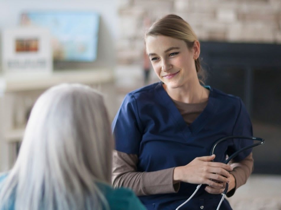 A nurse in a navy blue uniform talks with an elderly woman.