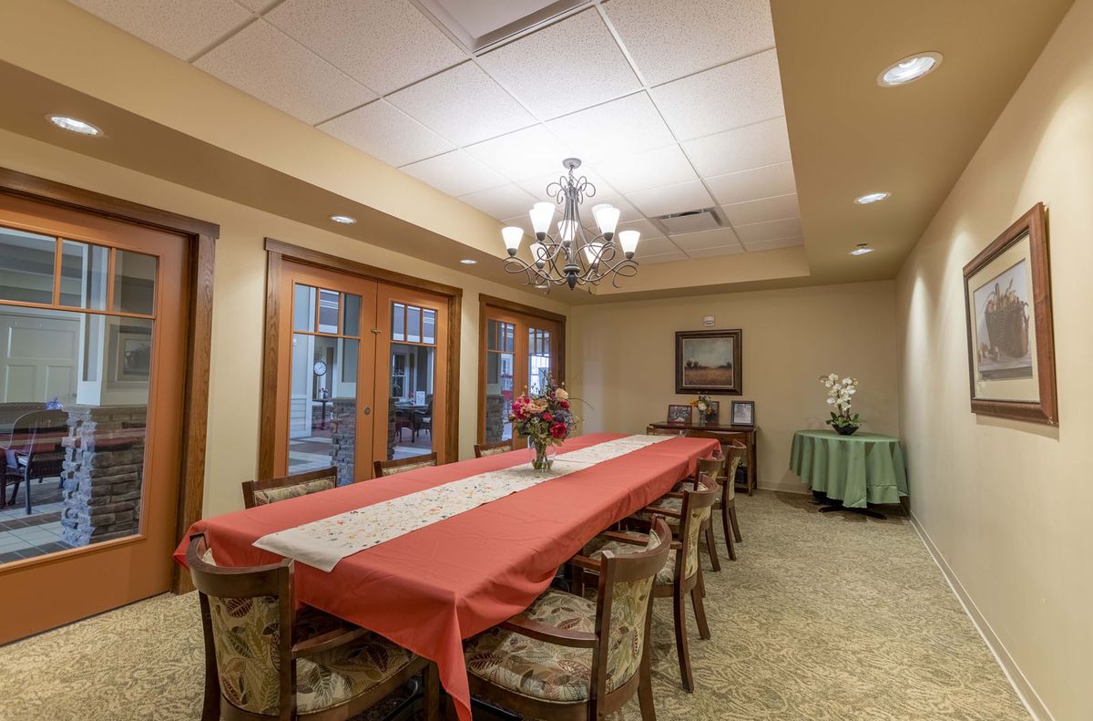 A well-decorated dining room with a long table and chairs, featuring a chandelier and floral centerpieces.