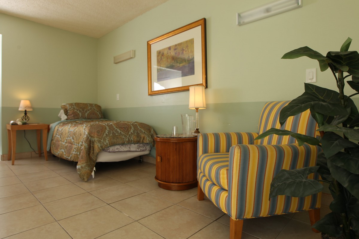 A cozy bedroom with a single bed, striped armchair, and nightstand with a lamp.
