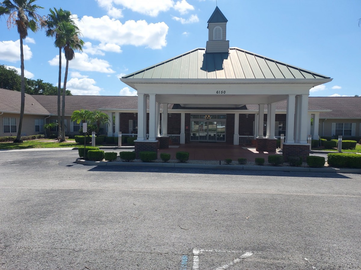 A building entrance with a driveway lined by palm trees under a sunny sky.