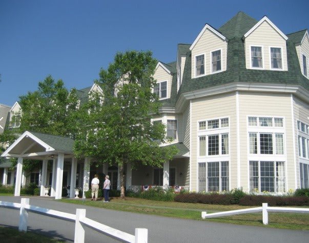 A large building with multiple windows and a green roof, surrounded by trees on a sunny day.