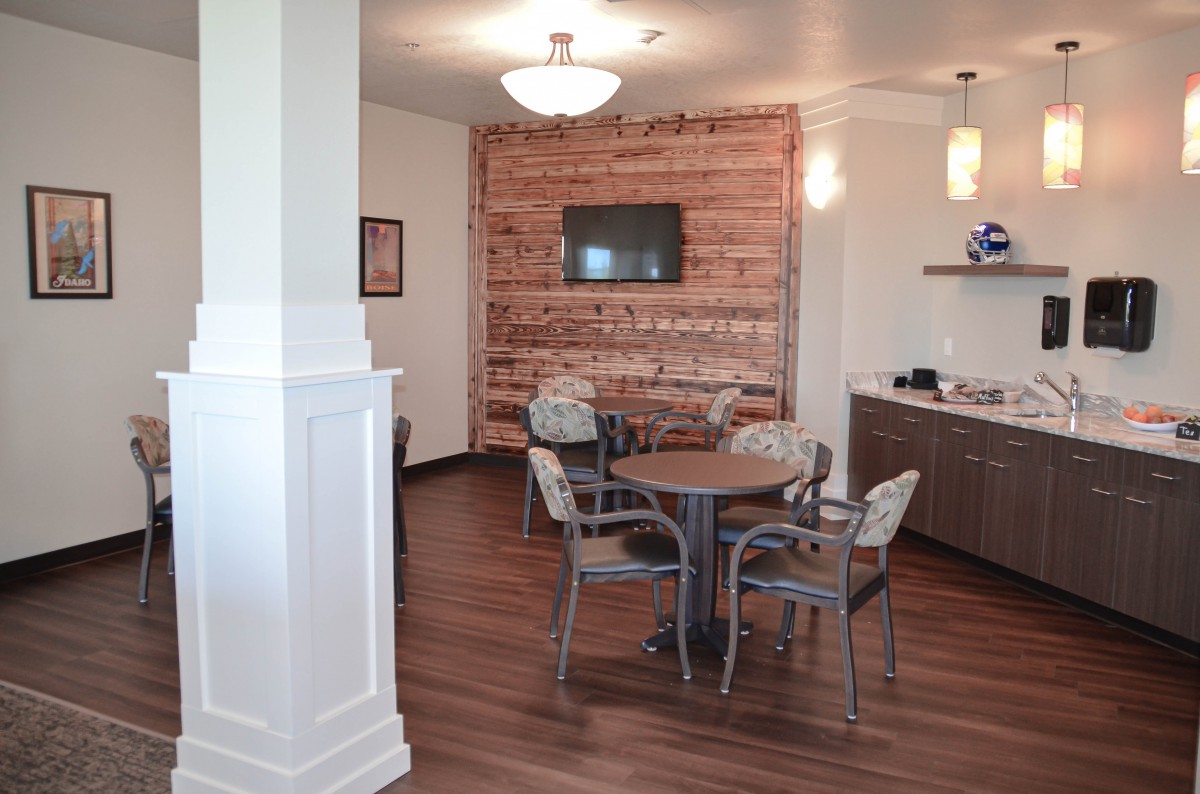 A cozy dining area with a wooden table, chairs, and a brick accent wall, featuring a mounted TV and modern lighting.