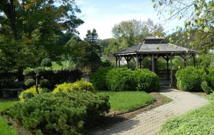 A serene garden with a wooden gazebo surrounded by lush greenery and a brick pathway.