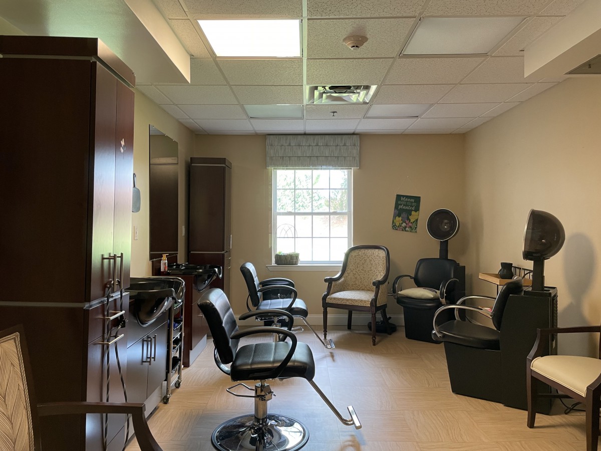 An empty hair salon with several chairs and styling equipment arranged around a brightly lit room.