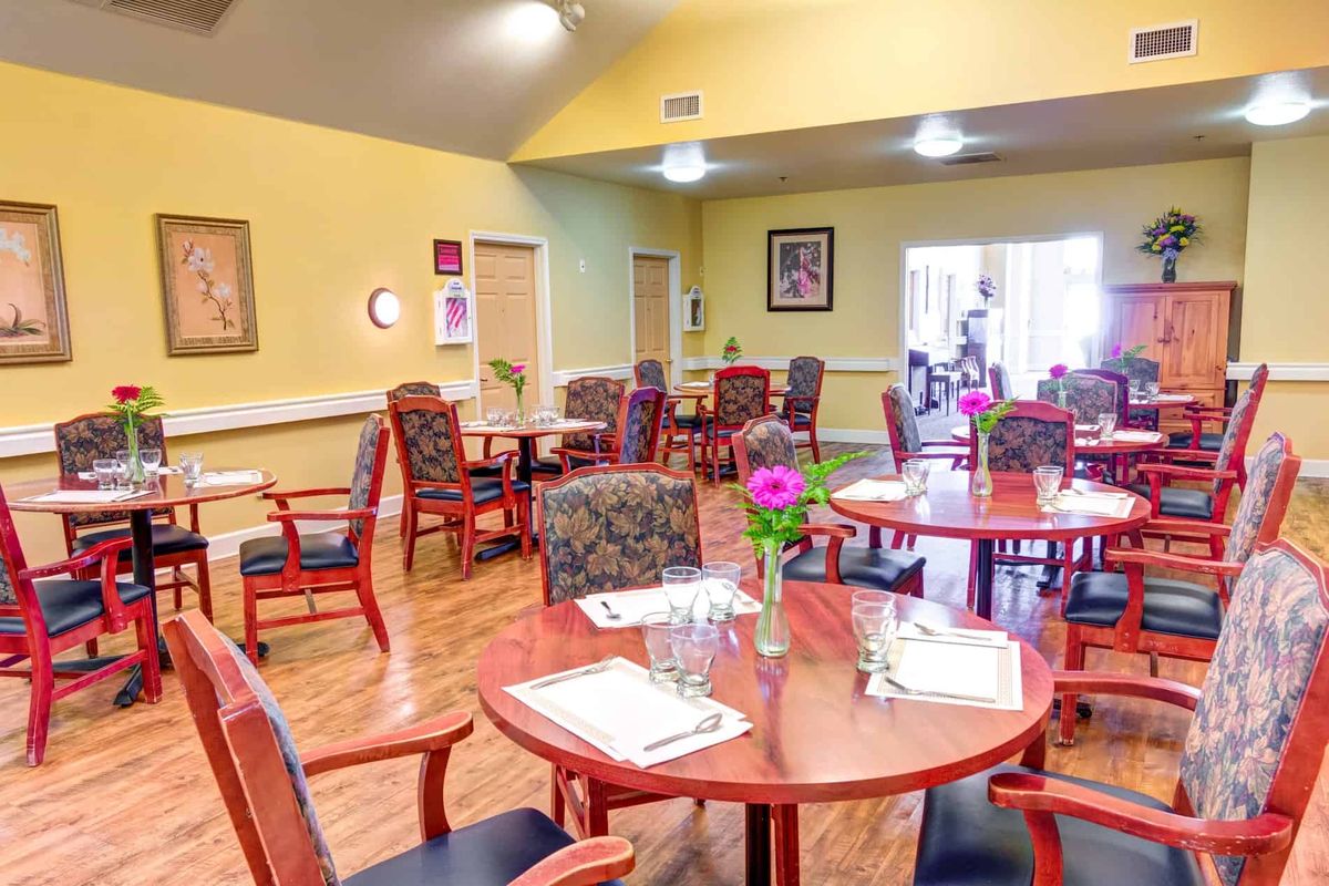 A cozy dining room with neatly arranged tables and chairs, featuring floral decorations on each table.