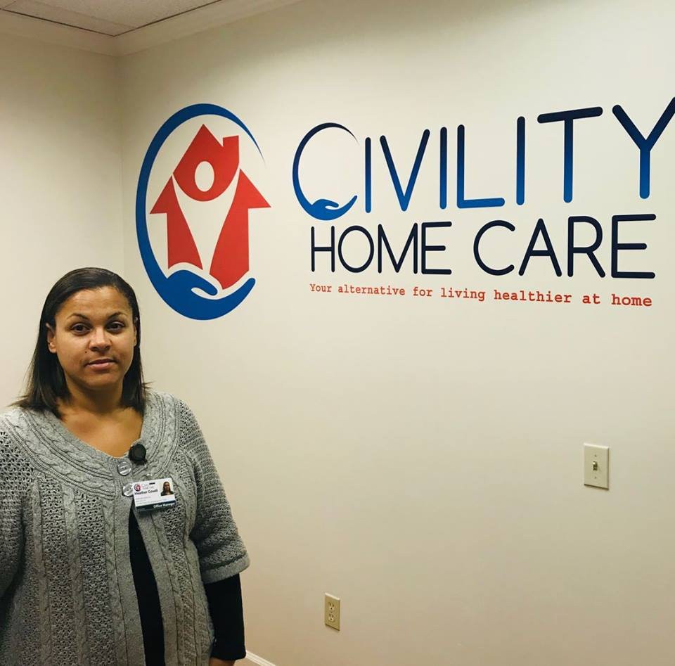 A woman stands in an office beside a wall featuring the Civility Home Care logo.