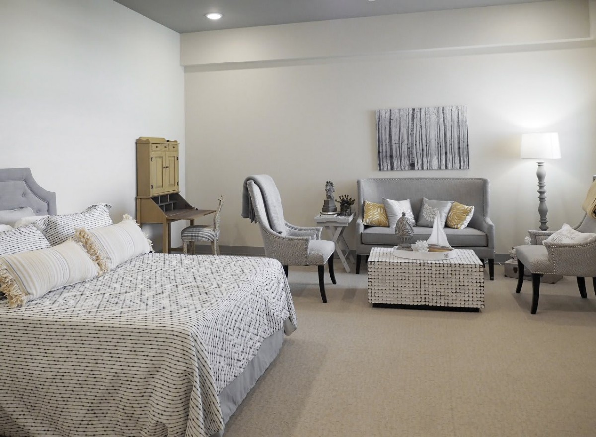 A modern bedroom with neutral tones, featuring a bed, armchair, sofa, and decorative elements.