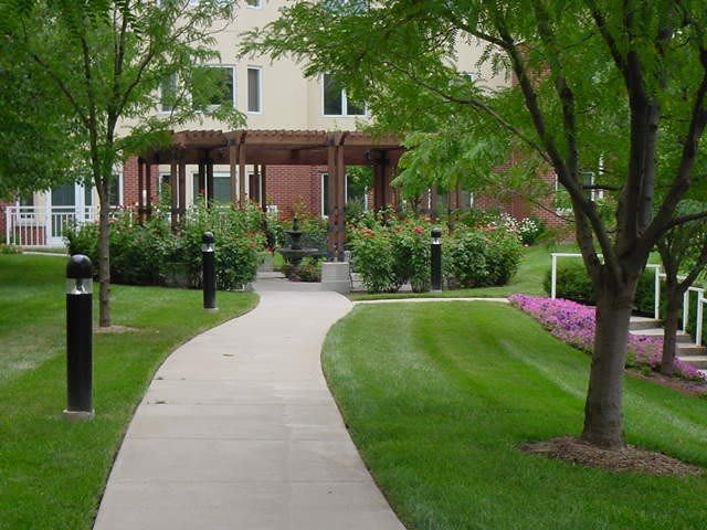 A serene walkway surrounded by lush greenery and vibrant flowers leading to a building in the background.
