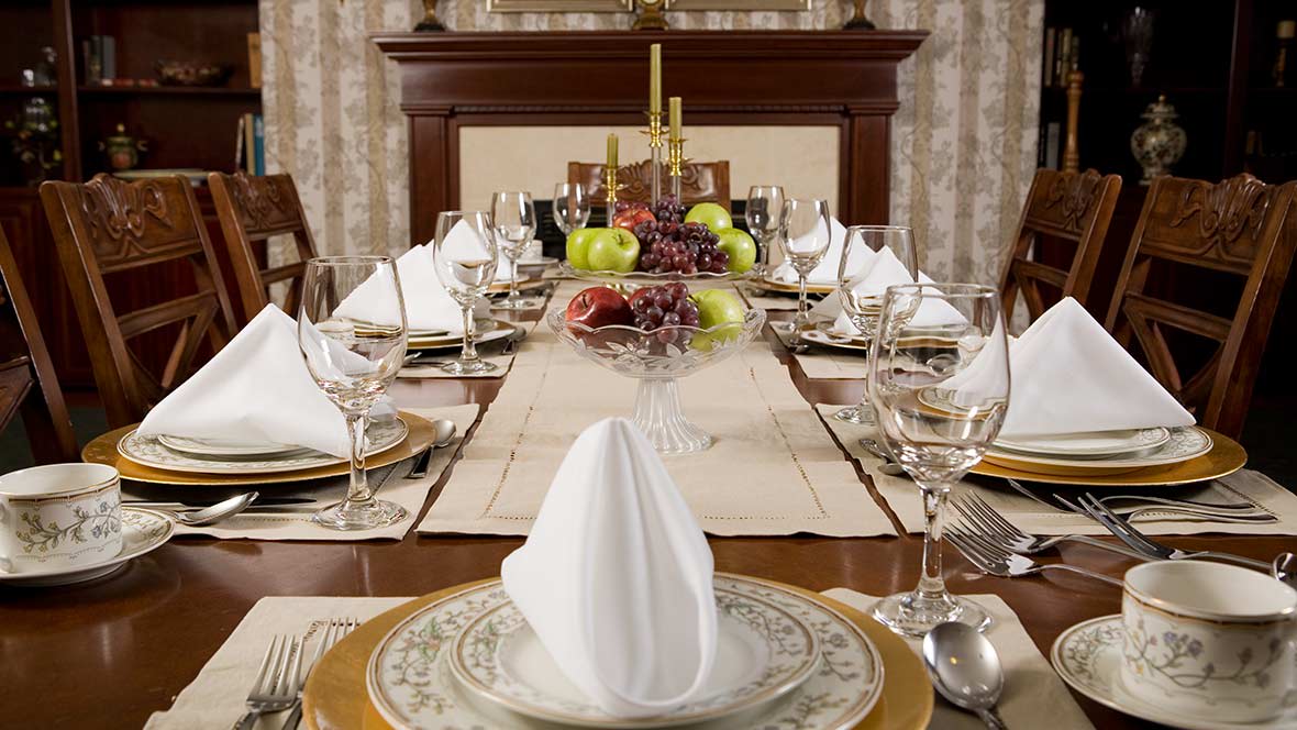 A formally set dining table with elegant dinnerware and a decorative centerpiece.