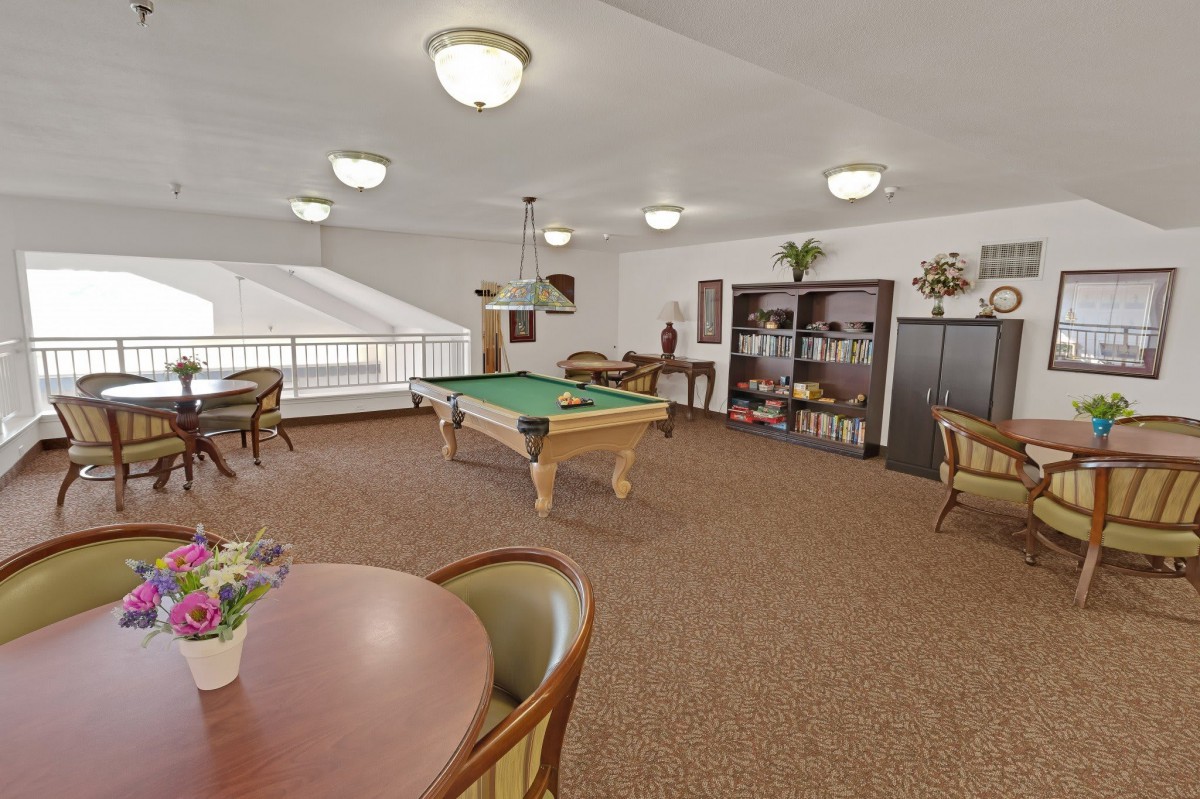 A spacious and well-lit game room featuring a pool table, bookshelves, and comfortable seating.