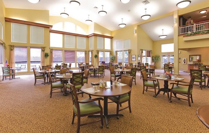 A spacious dining room with neatly arranged tables and chairs, featuring warm lighting.