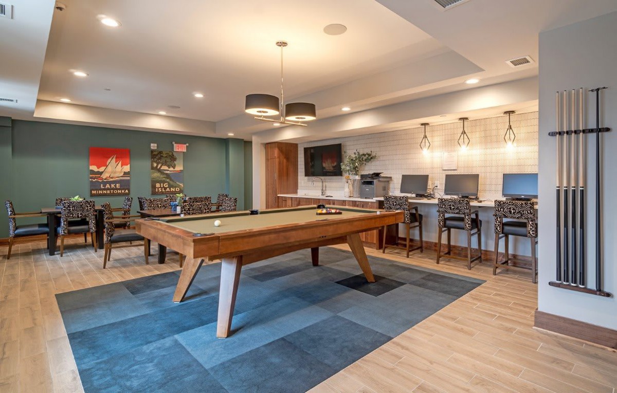 A modern game room featuring a pool table and lounge area with computers and stylish lighting.
