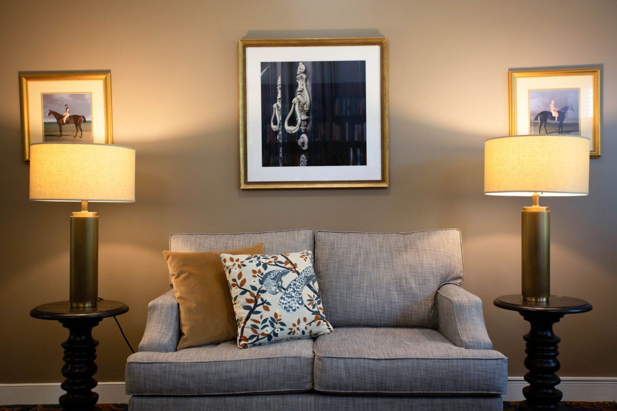 A cozy living room with a gray sofa, accented with patterned cushions and flanked by two warm-lit lamps. An abstract artwork hangs above the seating area.