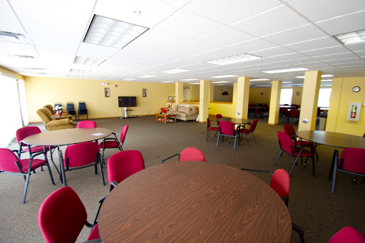 A spacious meeting room featuring round tables and red chairs, designed for community gatherings.