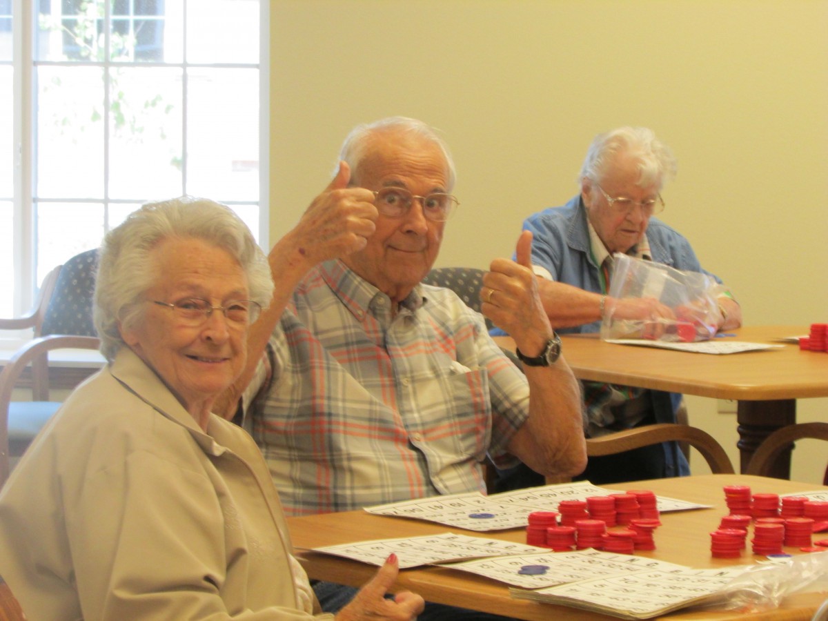 A group of senior citizens enjoying a game of bingo, with one giving a thumbs up gesture.