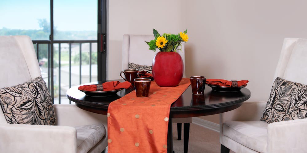 A beautifully set dining table with orange accents and a vase of sunflowers as the centerpiece.