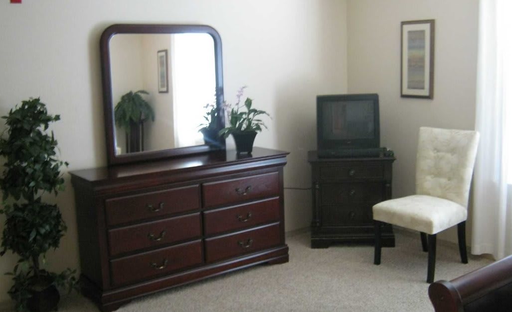 A bedroom with a dresser and mirror next to a vintage television.