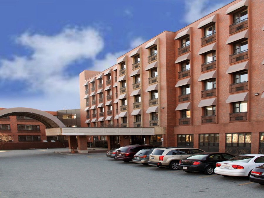 A large brick hotel building with multiple floors and a parking lot filled with cars.