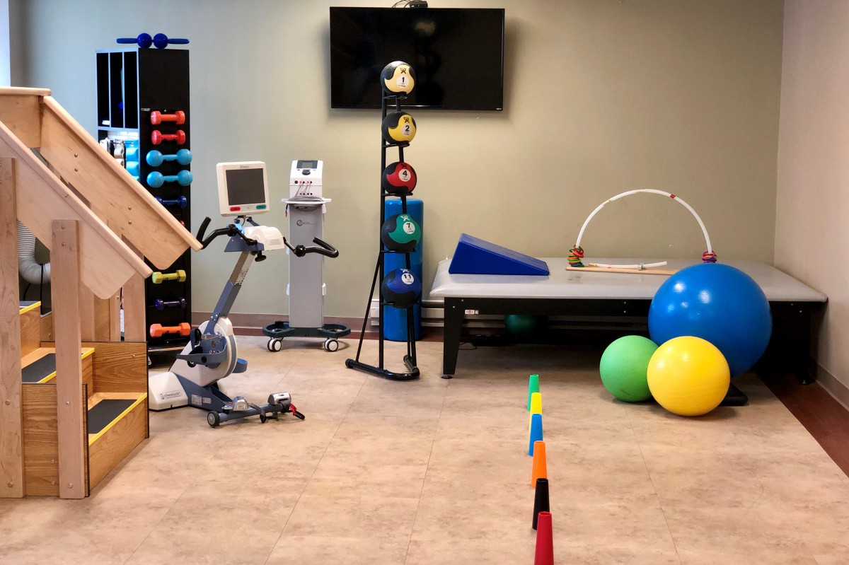 A physical therapy room equipped with exercise and rehabilitation tools, including fitness balls and an exercise bike.
