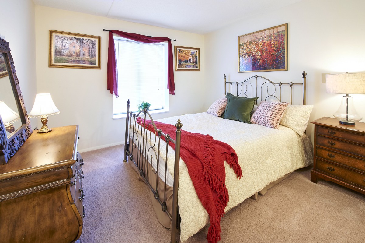 A cozy bedroom with a metal bed frame, decorative pillows, artwork on the walls, and a window with red curtains.