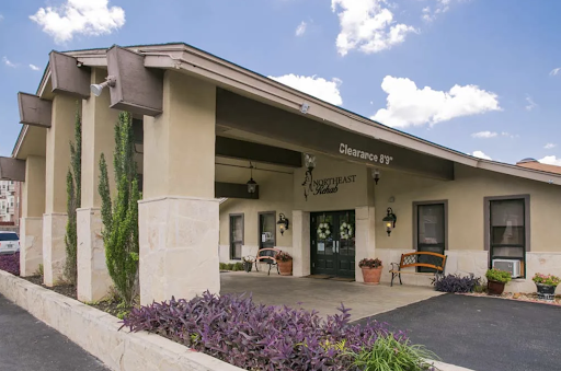 A welcoming entrance of a building, surrounded by beautiful landscaping under a blue sky.