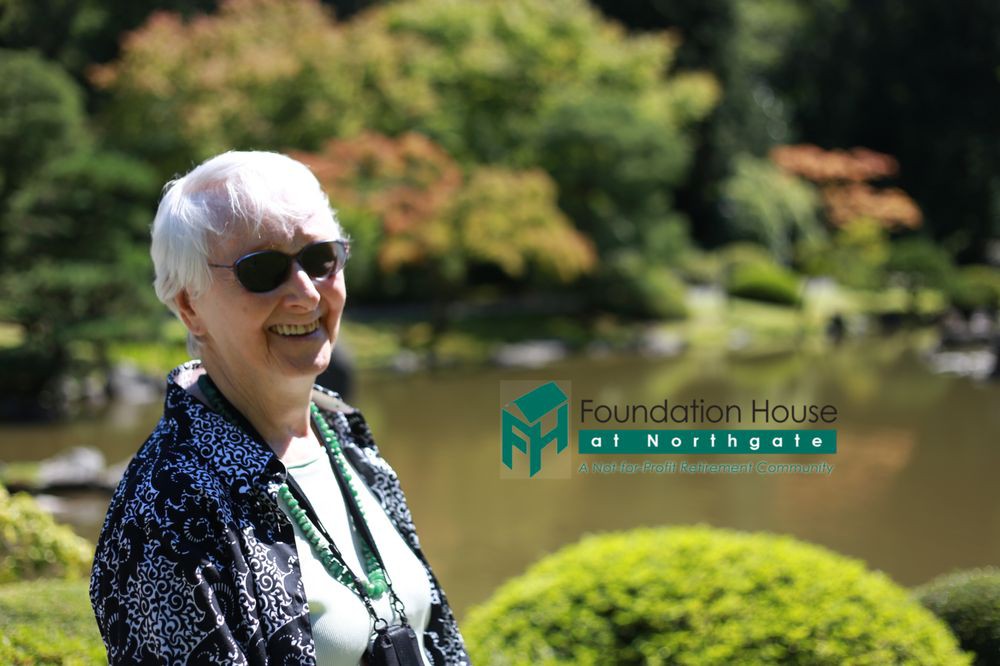An elderly woman wearing sunglasses enjoys a sunny day in a lush garden.