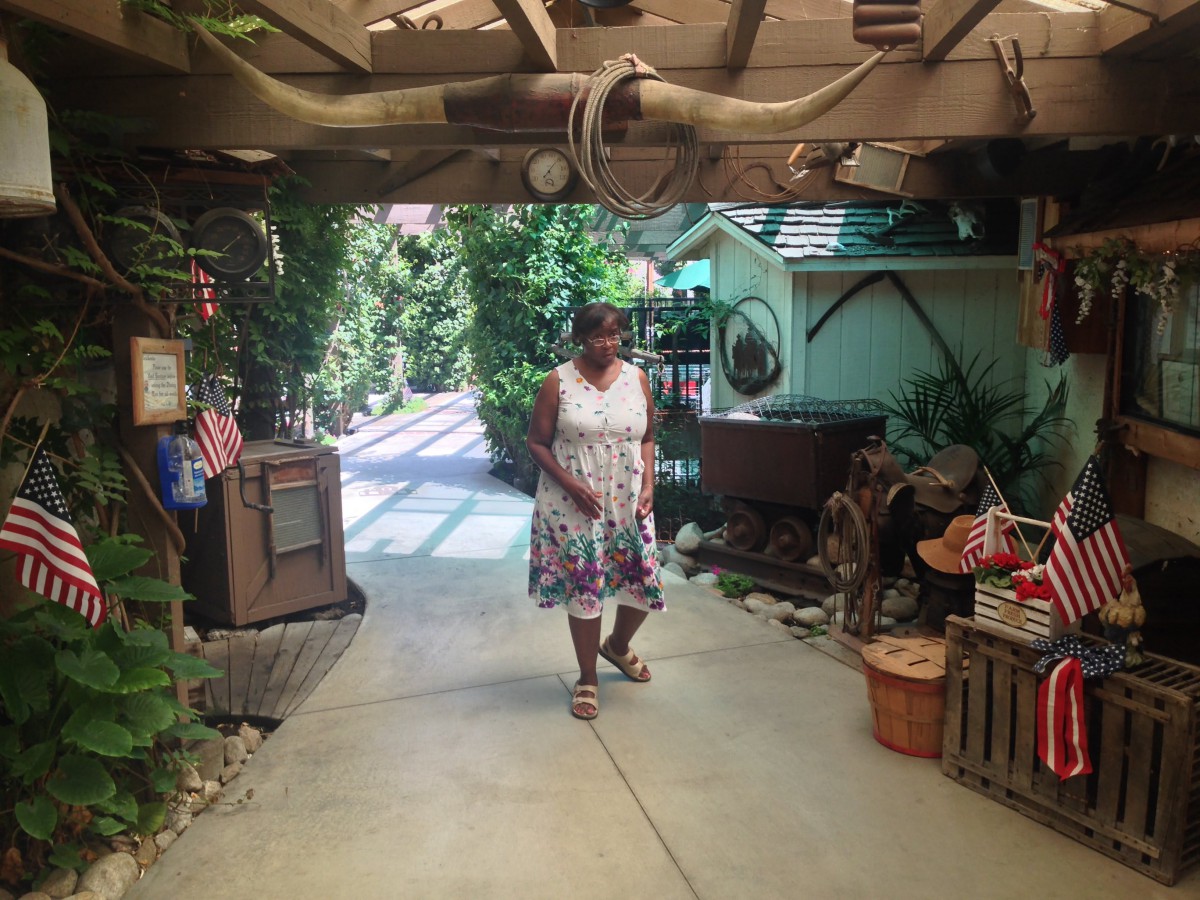 A woman in a summer dress walks down a shaded garden pathway surrounded by greenery.