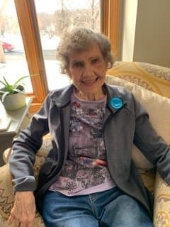 An elderly woman smiling while seated comfortably indoors.