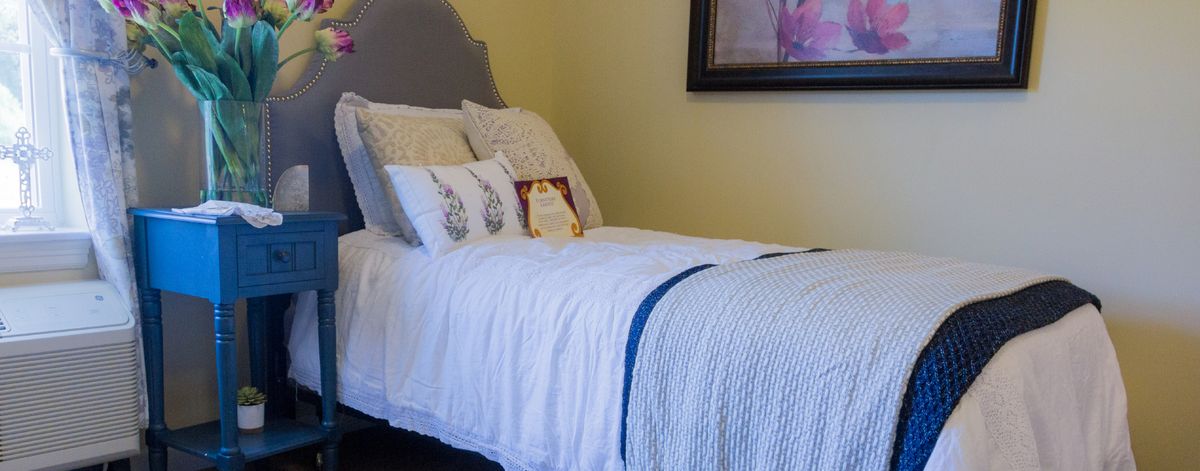 A neatly made bed in a cozy bedroom with decorative pillows and a painting on the wall.