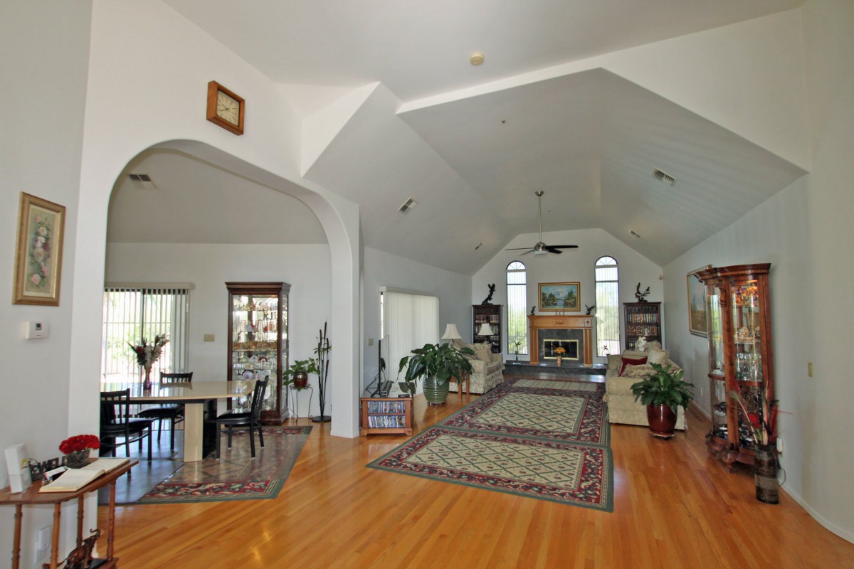 A spacious living room with vaulted ceilings, hardwood floors, and a cozy fireplace surrounded by large windows.