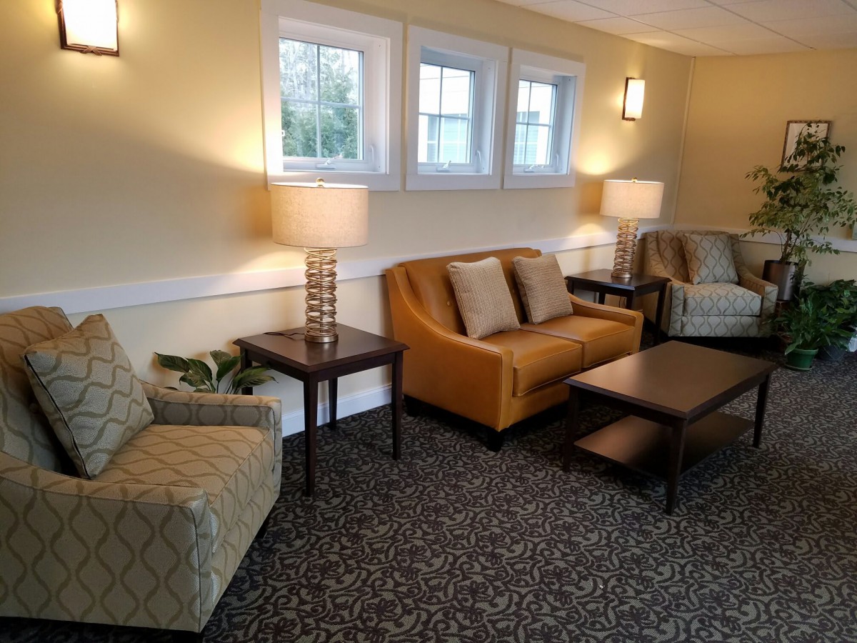A cozy living room with sofas, armchairs, lamps, and a carpeted floor.