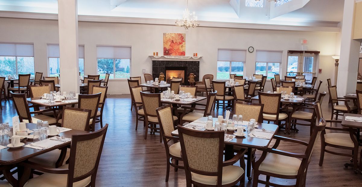 A well-lit dining room with neatly arranged tables and chairs, featuring a central fireplace.
