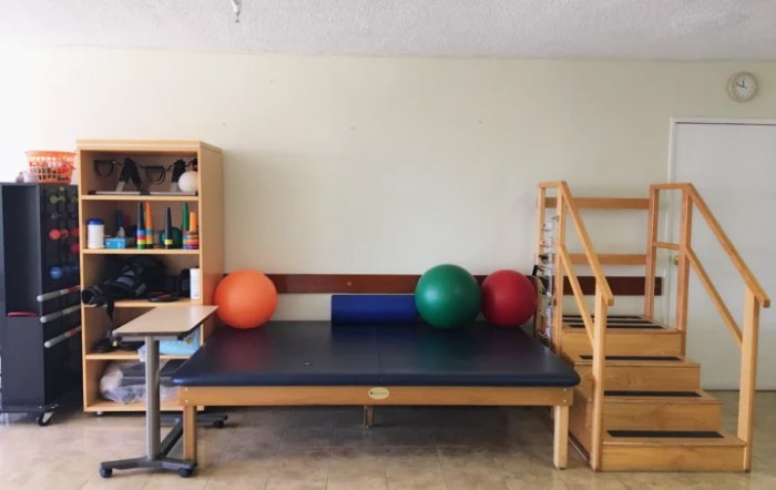 A physical therapy room with a treatment table, gym balls, and stairs for rehabilitation exercises.