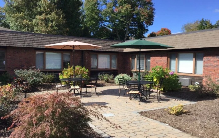 A peaceful outdoor patio area with tables, chairs, and umbrellas set against a brick building.