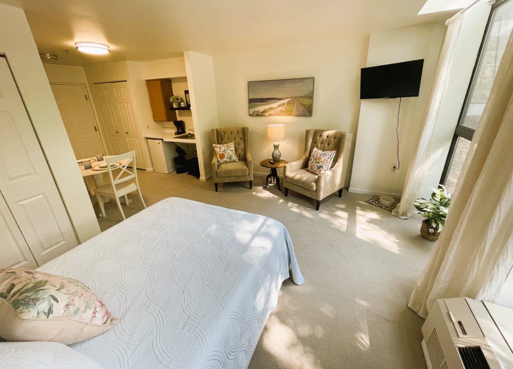 A cozy bedroom with a bed, armchairs, and a small TV, featuring soft lighting and elegant decor.