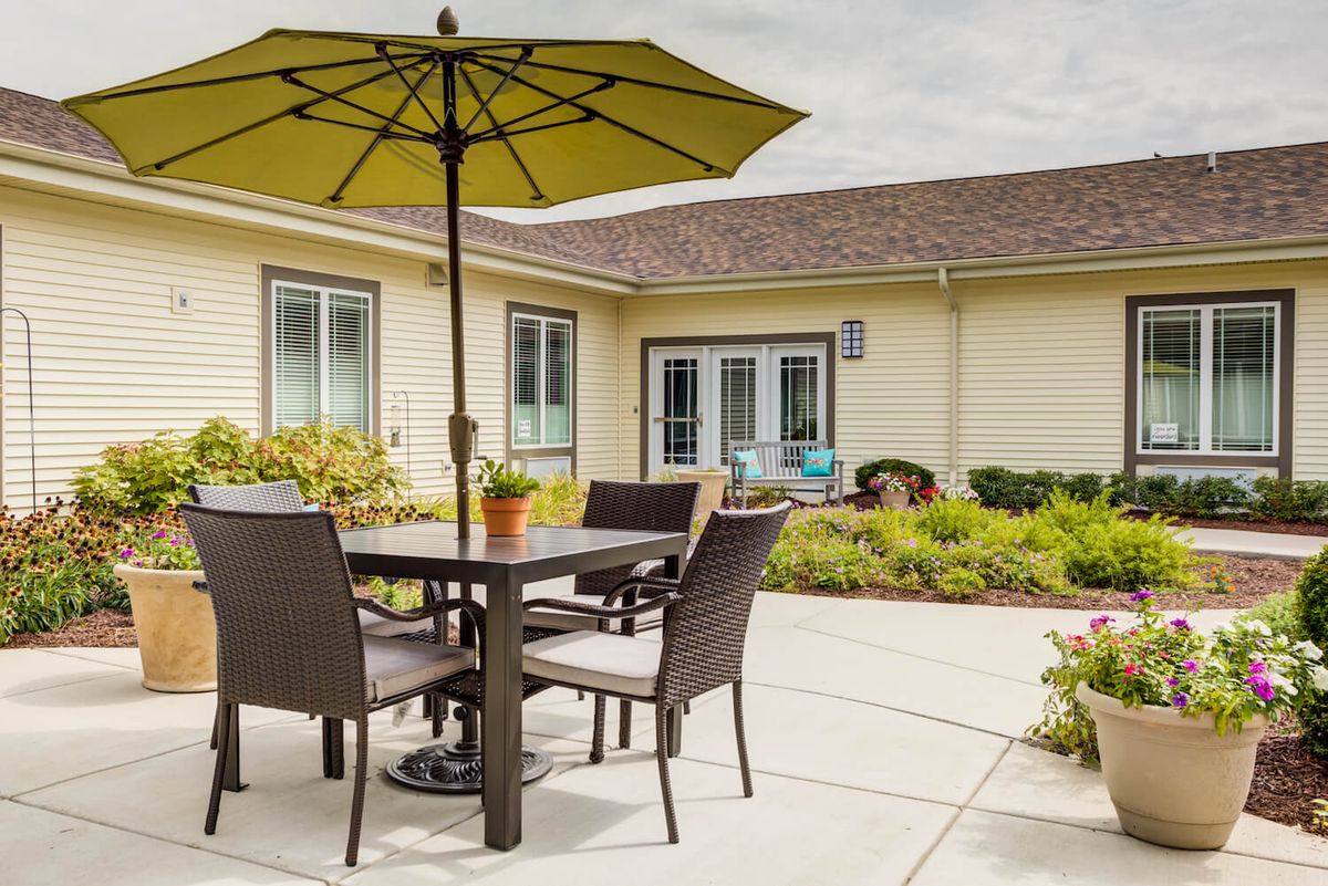 A cozy patio with a table and chairs set under a large umbrella, surrounded by a landscaped garden.
