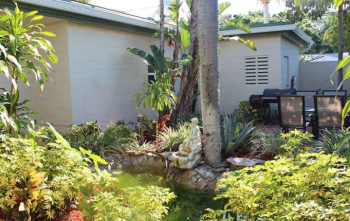 A lush tropical garden featuring a variety of plants, a palm tree, and a small statue.