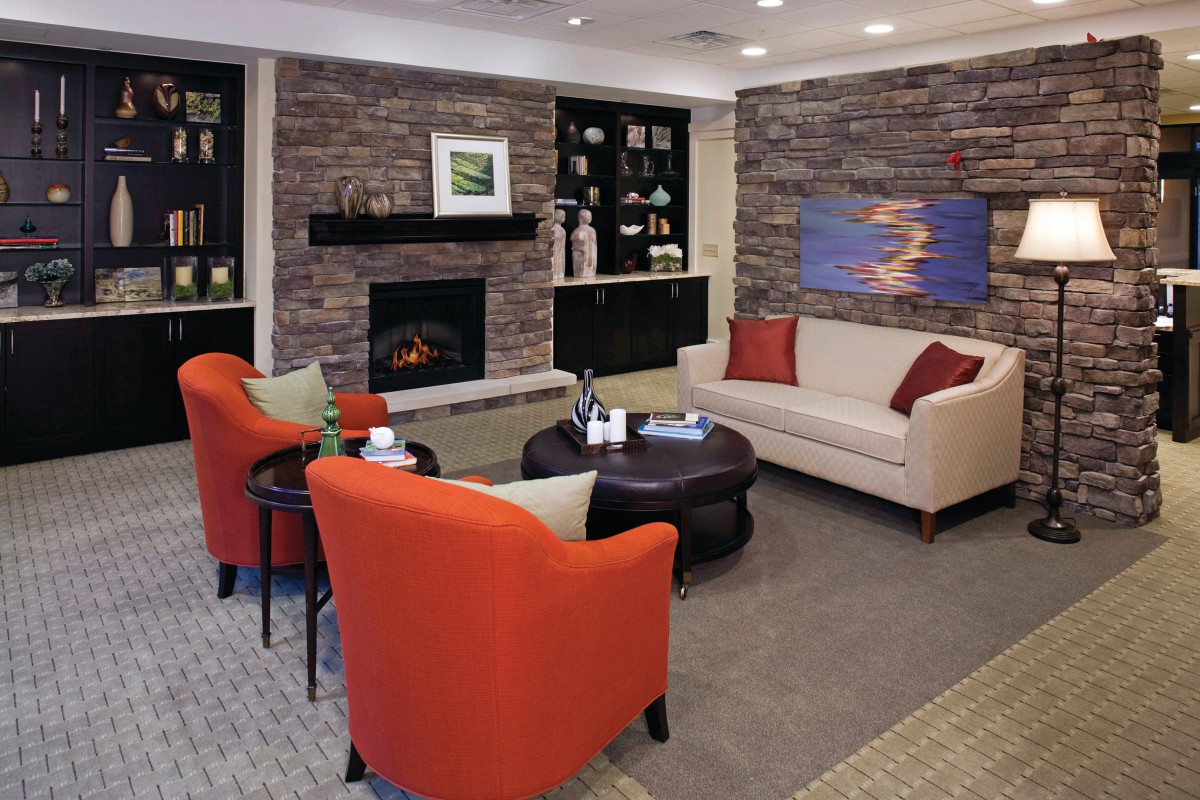 A modern living room featuring a stone fireplace, orange chairs, and a cozy sofa.