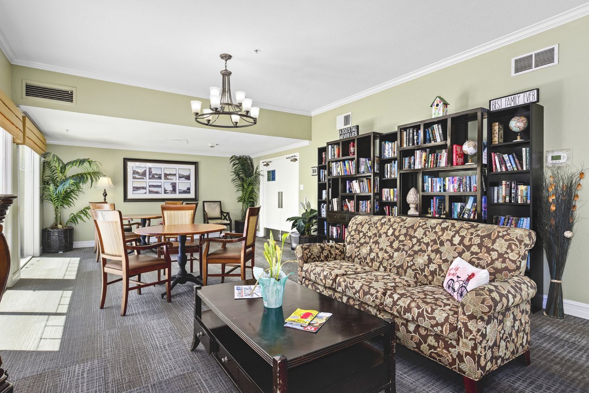 A cozy living room with a patterned sofa, bookshelves, and a dining area under a chandelier.