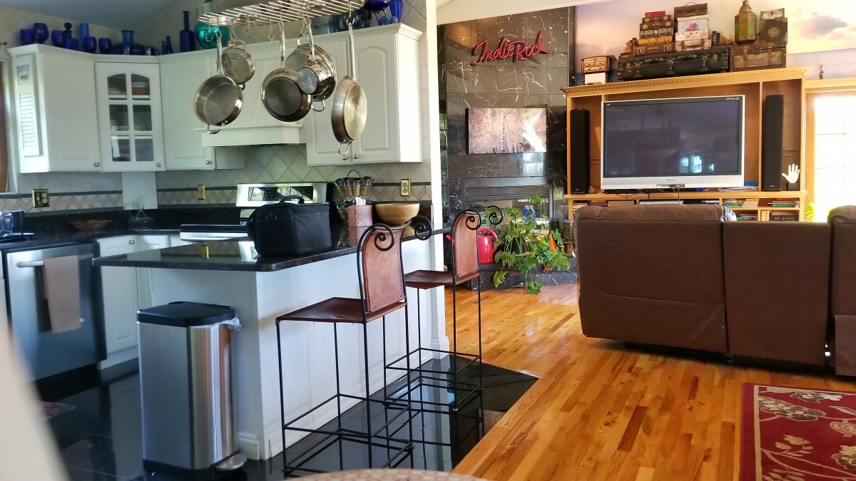 A modern kitchen with bar stools and an open living area, featuring hardwood floors and hanging pots.