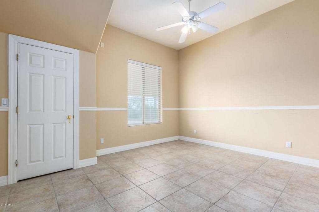 An empty room with beige walls, a tile floor, a window, and a ceiling fan.