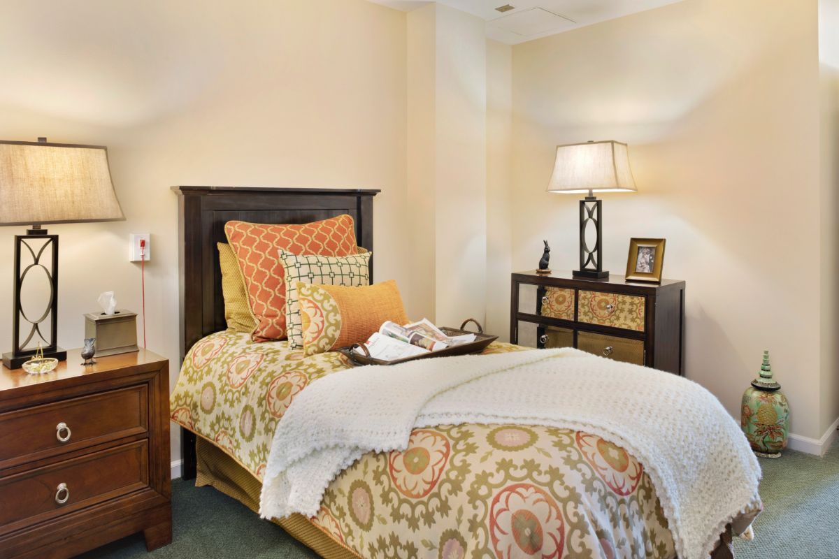 A cozy bedroom with decorative pillows, a bedside lamp, and warm lighting.