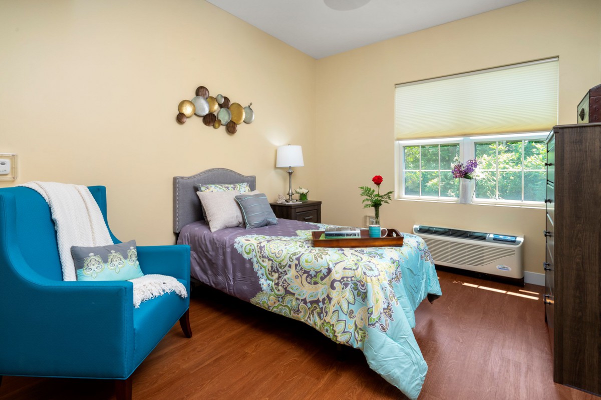A cozy bedroom featuring a single bed with a floral bedspread, an armchair, and decorative wall art.