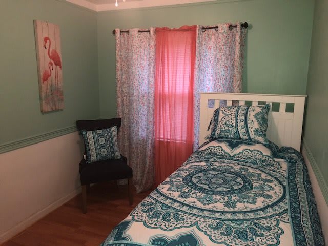 A cozy bedroom with turquoise bedding, decorated with colorful curtains and wall art.