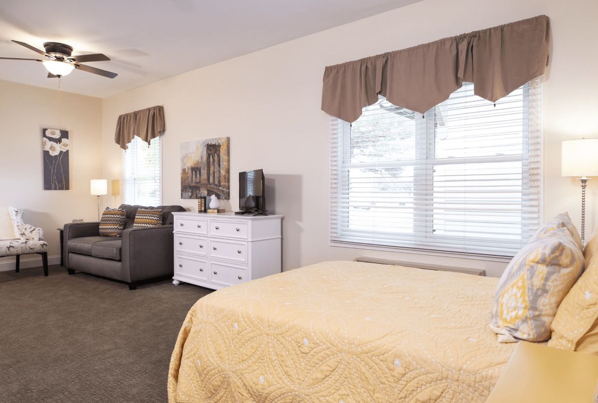 A cozy bedroom with a bed, dresser, and sofa arranged near two large windows.
