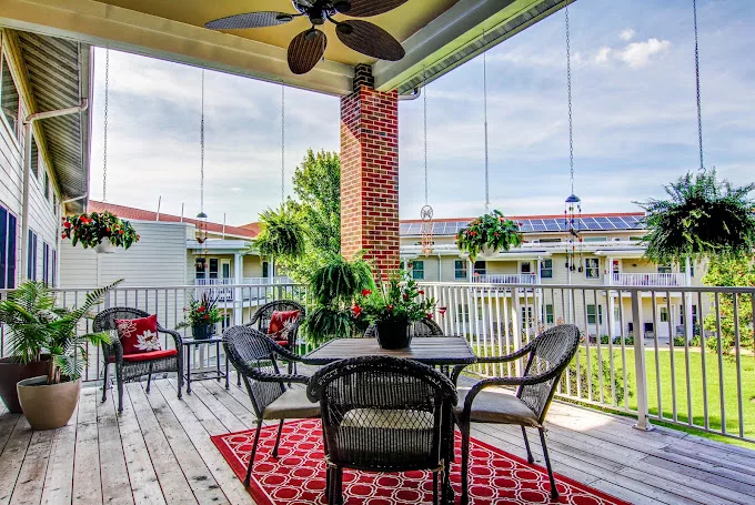 A cozy patio with outdoor furniture, hanging plants, and a red rug, perfect for relaxation.