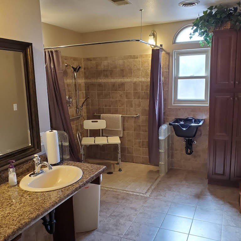 An accessible bathroom equipped with a shower area, sink, and tiled flooring.